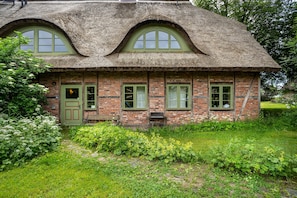 Ein traditionelles Backsteingebäude mit einem Strohdach, grünen Fenstern und einem kleinen Garten.