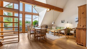 A spacious dining area with wooden furniture, large windows, and a view of greenery. - Apartment "Waldkauz" with Private Balcony (Putbus)
