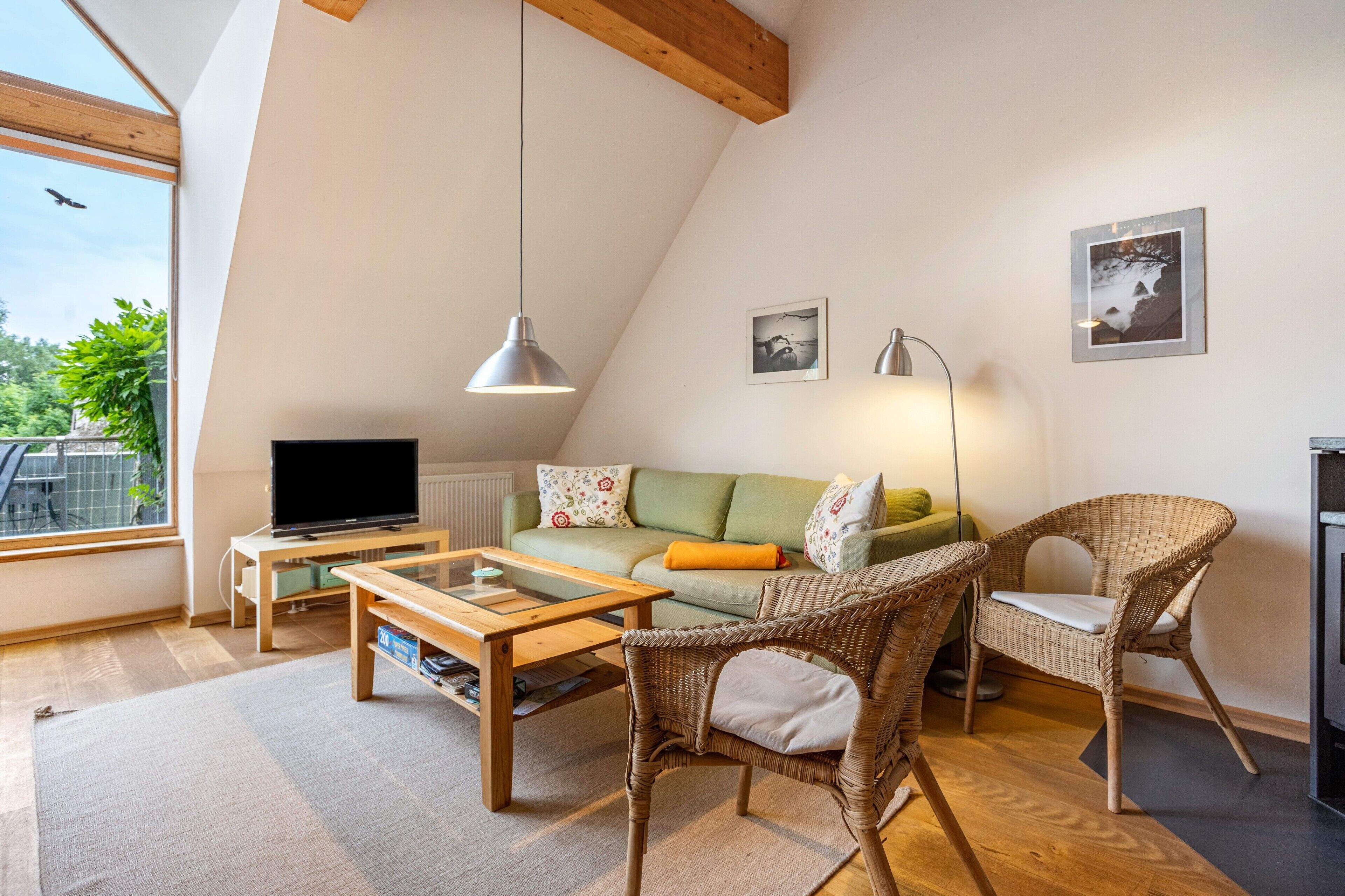 A loft-style living room with a television, sofa, wicker chairs, and artwork on the walls.