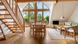 A spacious loft with a wooden staircase, a dining area with a table and chairs, a sofa, and a television. - Apartment "Waldkauz" with Private Balcony (Putbus)