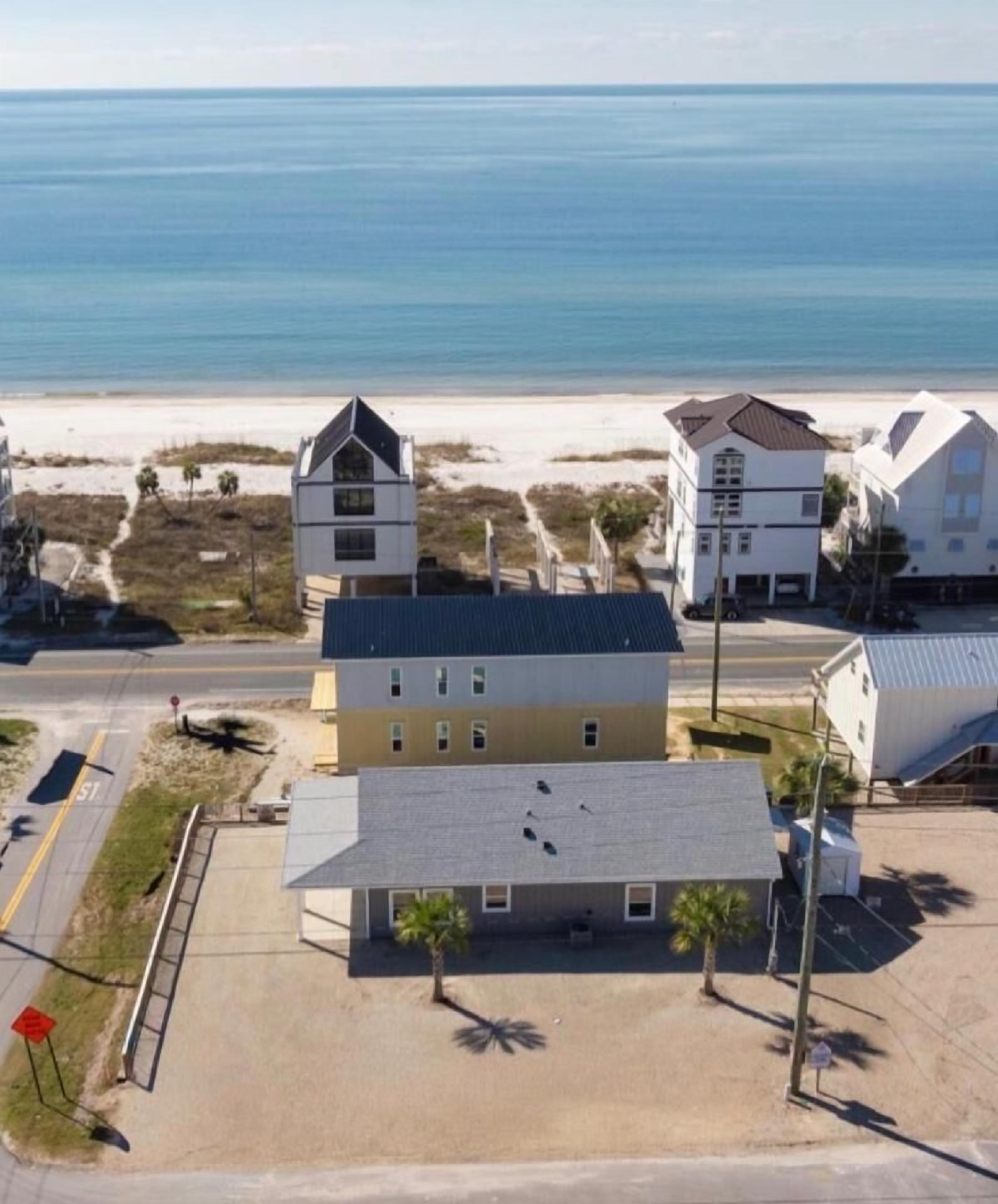 A beachfront property with a two-story building, a parking area, and a view of the ocean.