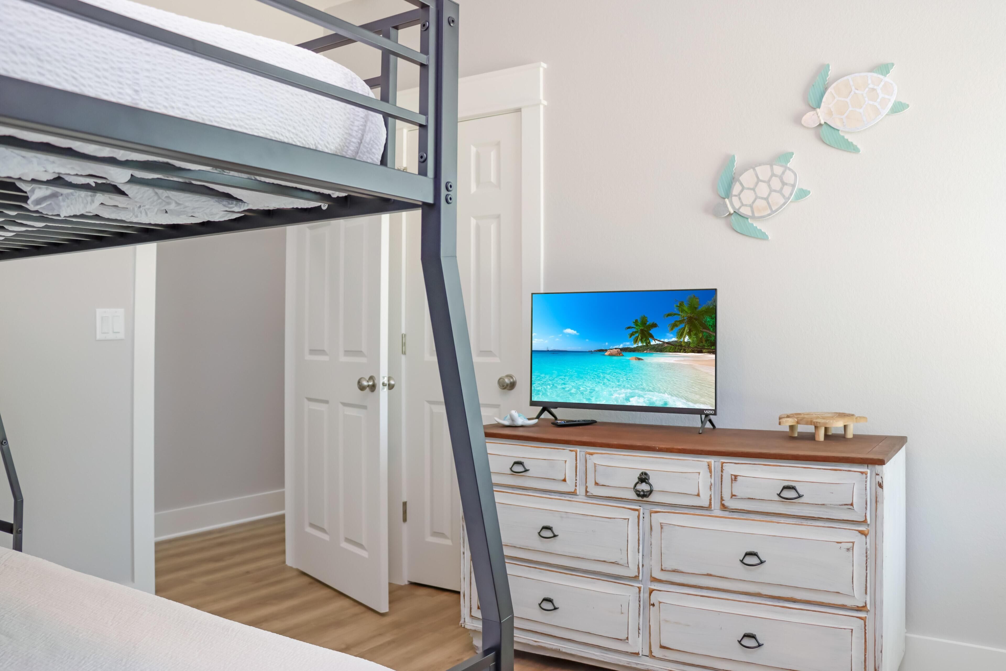 Un lit superposé avec un téléviseur posé sur une commode, une porte et un mur décoré de motifs représentant des tortues.