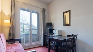 A room with a bed, a TV, a dining table with chairs, a window with curtains, and a view of the outdoors. - Apartment in Grasse With Swimming Pool (Grasse)