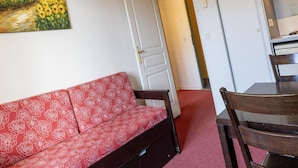 A room with a red patterned sofa, a wooden dining table, and a painting of a sunflower field on the wall. - Apartment in Grasse With Swimming Pool (Grasse)