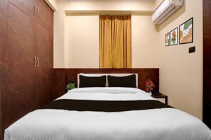Ein Hotelzimmer mit Bett, Nachttisch, Topfpflanze und Wandklimaanlage.
