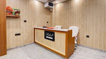 A reception desk with a sign, a wooden wall with vertical slats, and a ceiling-mounted air conditioning unit.