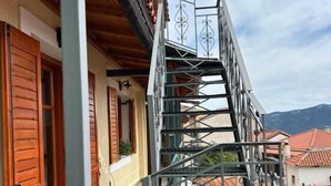 Una escalera metálica que lleva a un balcón con contraventanas de madera y vistas de los edificios circundantes.