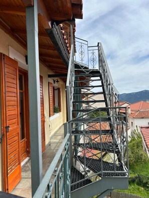 Una scala in metallo conduce a un balcone con persiane in legno e vista sugli edifici circostanti.