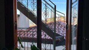 Un acceso a un balcón con barandilla metálica y vistas de un edificio con tejados de tejas rojas.