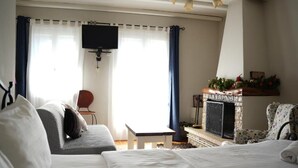 Un dormitorio con cama, una mesita, una silla, chimenea y televisión.