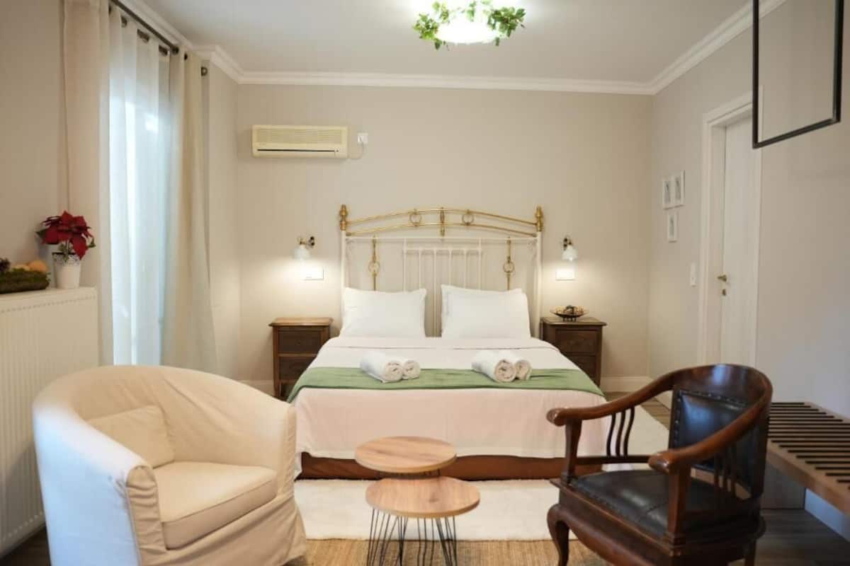 A bedroom with a bed, two bedside tables, a chair, a small table, and a radiator.