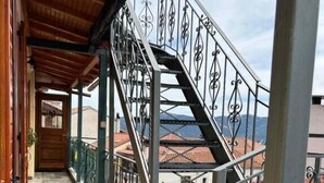 Un balcón cubierto con barandilla de metal, piso de piedra y vistas a edificios al fondo.