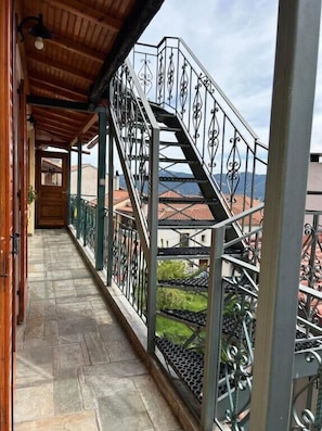 Un balcone riparato con ringhiera in metallo, pavimento in pietra e vista sugli edifici sullo sfondo.