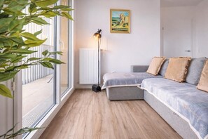 Una sala moderna con un sofá gris, un radiador, una lámpara de pie y un cuadro en la pared.