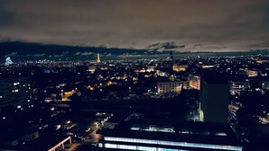 Paisagem urbana noturna com uma torre imponente e um edifício com grandes janelas voltado para a água.
