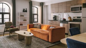 A modern kitchen with built-in appliances, a sofa, and a dining area. - Nester Finn Square Victoria (Montréal)