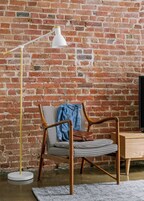 A chair with a houndstooth pattern, a denim jacket, and a brown leather bag against a brick wall.