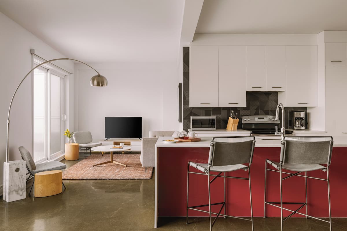 A modern kitchen with white cabinets, a red island, and bar stools.