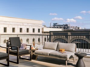 Una terraza en la azotea con mobiliario exterior, una mesa y vistas a la ciudad.