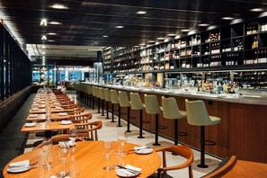 Un restaurante con largas mesas de madera, taburetes de bar y estanterías llenas de botellas.