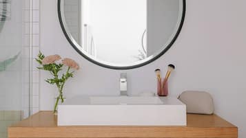 A bathroom with a white sink, a round mirror, a vase with flowers, and a wooden vanity.