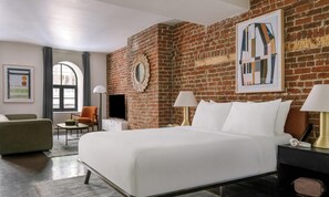 Una habitación de hotel con pared de ladrillo, cama, televisor, sillón y obras de arte en las paredes.
