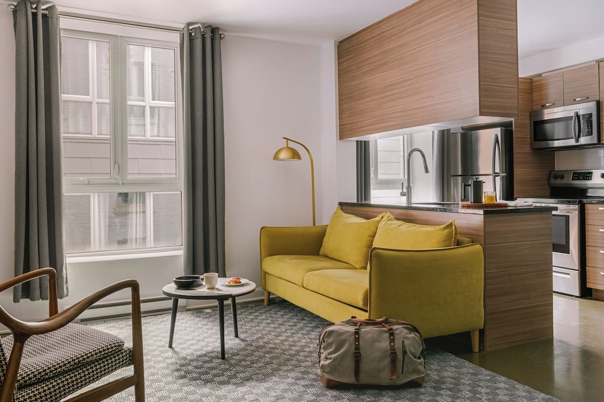 A modern living room with a sofa, a small table with a cup, a lamp, and a suitcase.