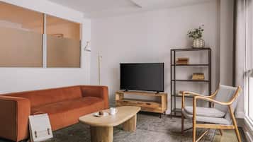 Una sala de estar con un sofá, una mesa de centro, un televisor, una silla, una estantería y un ventanal.
