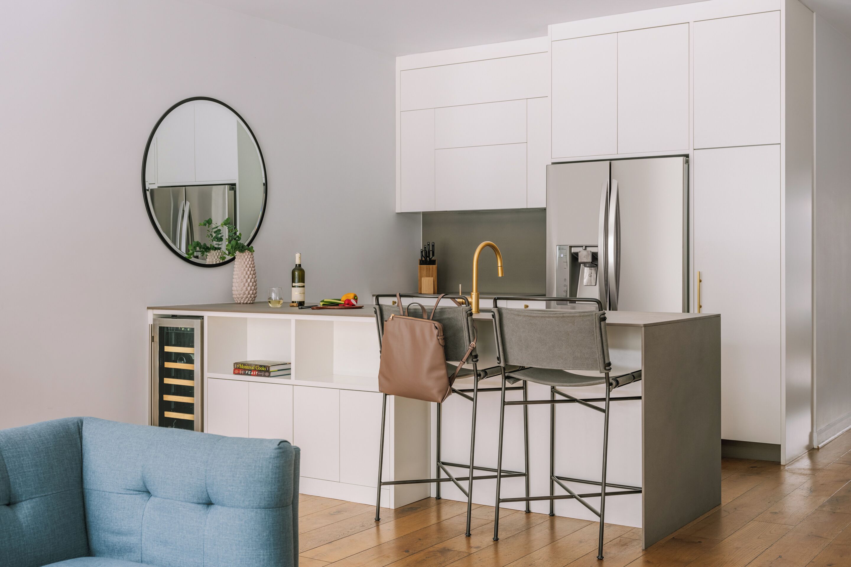 A modern kitchen with white cabinets, a round mirror, a bar stool, and a blue chair.