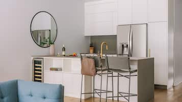 A modern kitchen with white cabinets, a round mirror, a bar stool, and a blue chair.