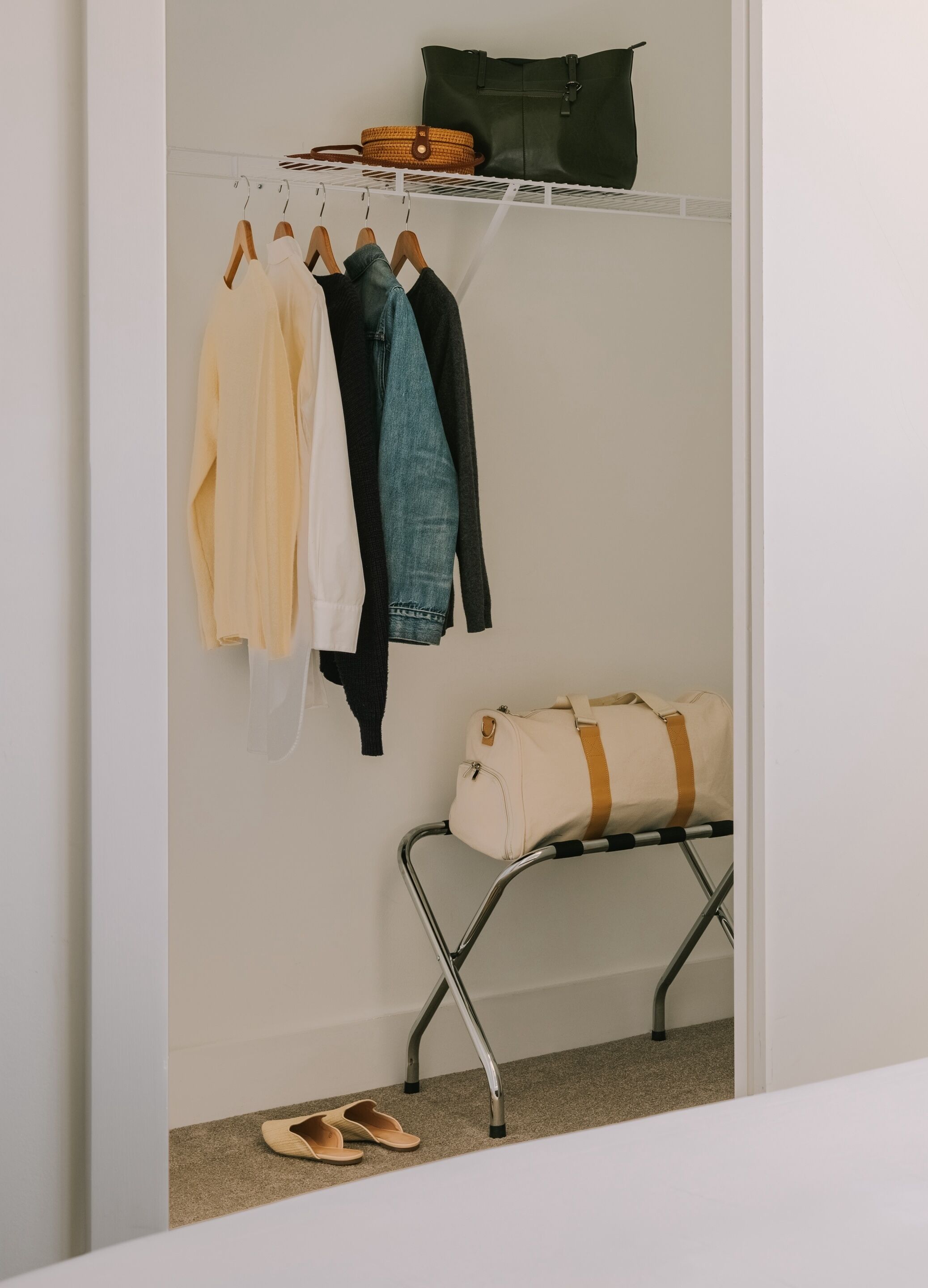 Ein Schrank mit aufgehängter Kleidung, eine zusammengefaltete Tasche auf einem Regal und ein Paar Schuhe auf dem Boden.