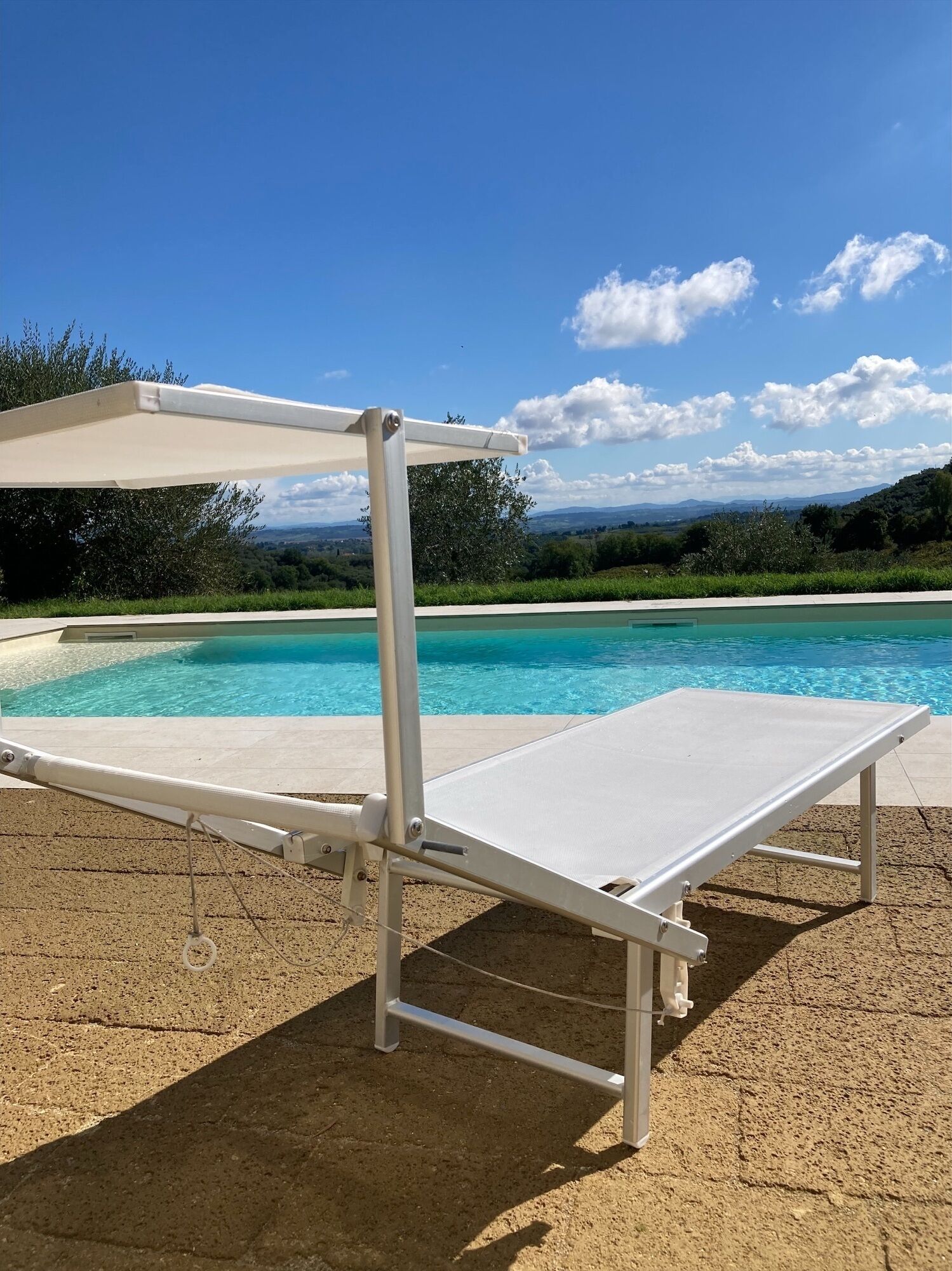 A white sun lounger by a pool with a clear view of the landscape.