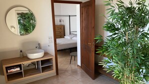 Un baño con un espejo redondo, un lavamanos blanco, un mueble de tocador de madera y una planta en maceta.