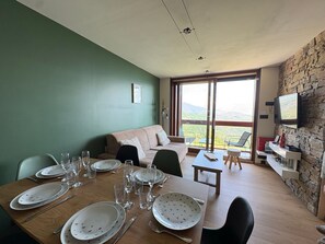 Un comedor con una mesa de madera dispuesta para una comida, un sofá y un televisor montado en una pared de piedra.