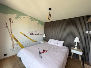 Un dormitorio con cama, un mural en la pared, una mesita de noche y una lámpara.