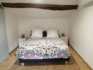 Ein Bett mit einer farbenfrohen, gemusterten Tagesdecke, weißen Kissen und einem Holzkopfteil.