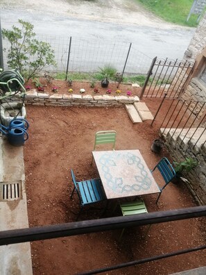 Une terrasse avec une table et des chaises, un jardin avec différentes plantes et un mur en pierre.