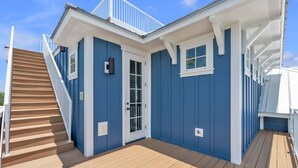 Un bâtiment bleu avec une terrasse en bois, une porte blanche et un escalier menant à un balcon.