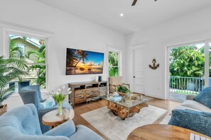 A spacious living room with a large window, a wooden coffee table, and a painting of a sunset. - Slice of Paradise by Duncan Real Estate (Holmes Beach)