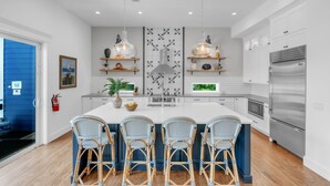 Une cuisine moderne dotée d’un îlot central, de tabourets de bar, de luminaires suspendus et d’appareils électroménagers en acier inoxydable.