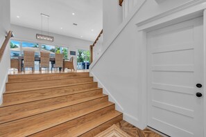 A wooden staircase leading to a white door, with wicker chairs and a view of greenery outside. - Slice of Paradise by Duncan Real Estate (Holmes Beach)