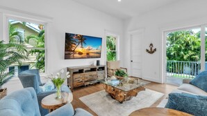Un salon spacieux avec une grande fenêtre, une table basse en bois et un tableau représentant un coucher de soleil.