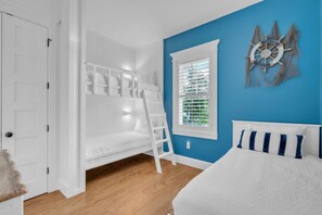 A bedroom with a bunk bed, a ladder, a window with blinds, a bed with a white headboard, and a blue wall. - Slice of Paradise by Duncan Real Estate (Holmes Beach)