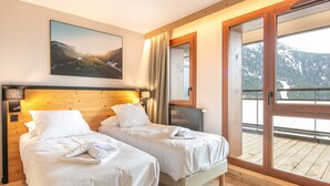 Camera d'albergo con due letti, un'ampia finestra vista montagna, un quadro appeso al muro e pavimento in legno.