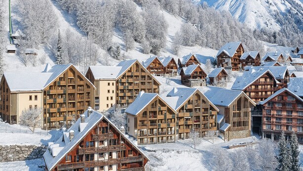 Una località montana innevata con chalet in legno e una pista da sci.