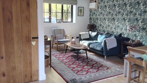 Ein Wohnzimmer mit Holztür, Sofa, Sessel, Couchtisch und einem gemusterten Teppich.