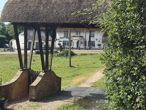Ein Gebäude mit einem Reetdach und einem Backsteinsockel, ein weißes Gebäude mit einem Schild, auf dem 'GREEN DRAW' steht, sowie ein Rasenstück mit einem Kiesweg.