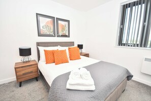A hotel room with a bed, two nightstands, a window with blinds, and two framed pictures on the wall. - Lovely 1 Bedroom Apartment in Leeds w WiFi (Leeds)