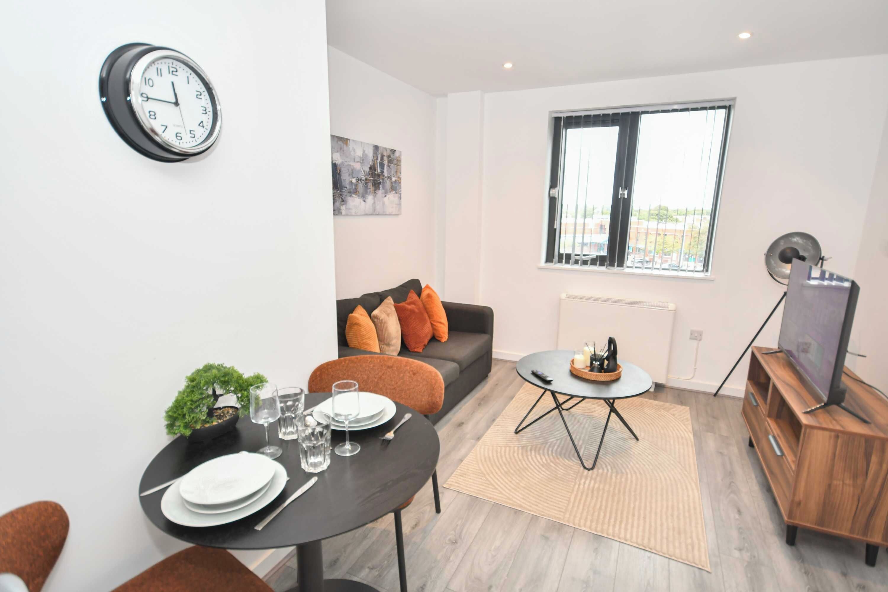 Ein modernes Wohnzimmer mit Essbereich, einer Couch mit Kissen, einem Couchtisch, einer Wanduhr und einem Fenster mit Blick.
