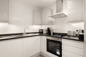 Una cocina moderna con armarios blancos, encimera negra, pileta de acero inoxidable, horno integrado y campana extractora.